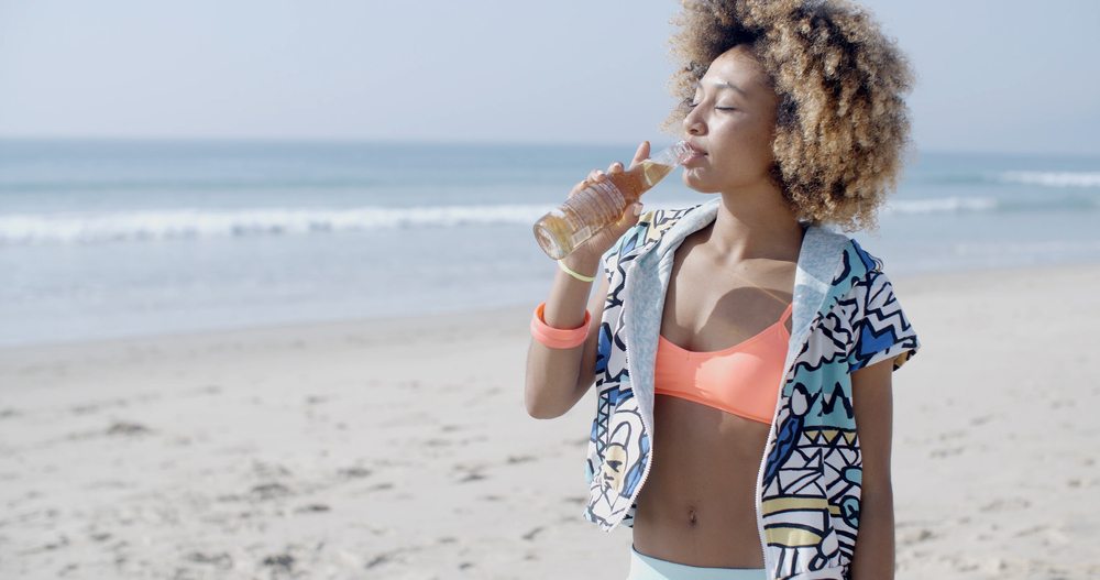 Young Woman Enjoying A Beer On A Sandy Beach