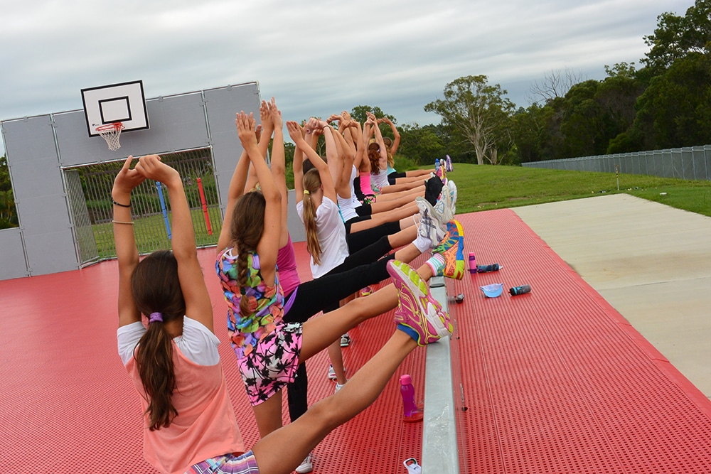 Women's Sporting group team stretching and exercising on the Multipurpose sports field, Staying in group accommodation at Brisbane Holiday Village